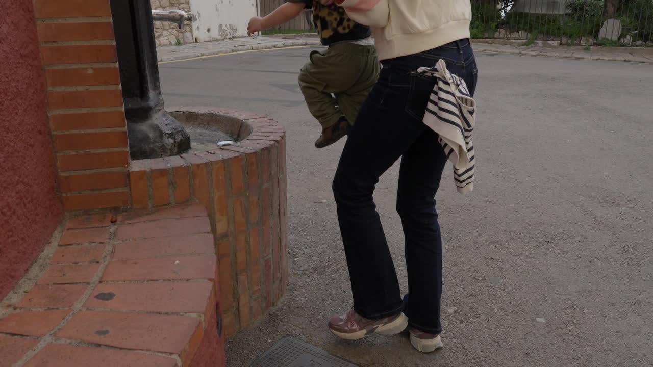 Mother picks ups toddler and puts him on to of a red brick wall