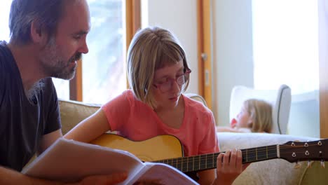 Vater-Hilft-Seiner-Tochter-Beim-Gitarrespielen-Im-Wohnzimmer-4k