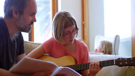 father helping her daughter to play guitar in living room 4k