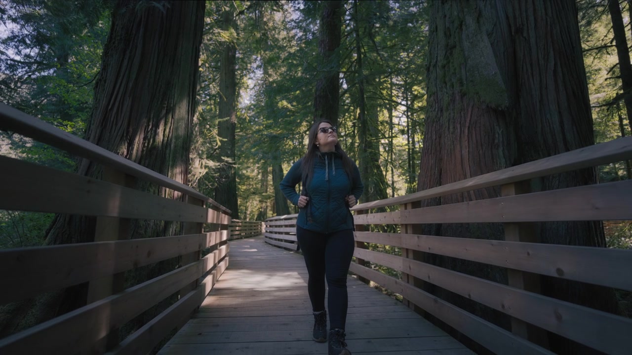 Young hiker woman with a backpack walking along the boardwalk in the woods