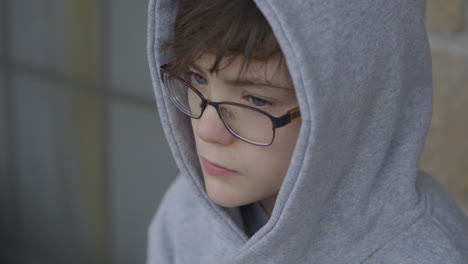 un chico lindo con una capucha gris y gafas esperando afuera mira a su alrededor, cerrado