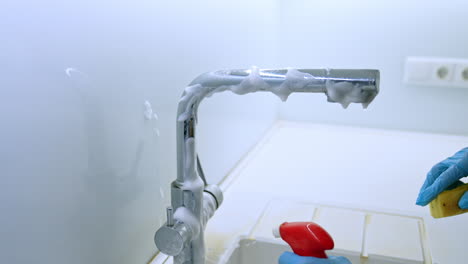 foam spray for faucet cleaning. a person wearing gloves cleans a kitchen faucet using foam spray, ensuring a shiny, hygienic finish