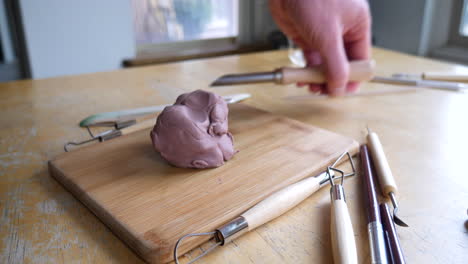 an artist preparing his sculpting tools and cutting a piece of brown modeling clay as he begins his project in the art studio