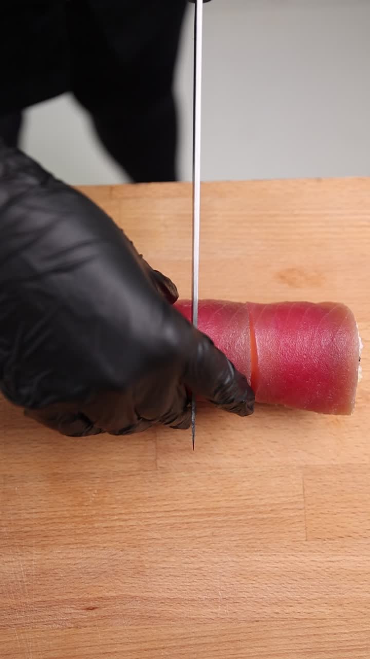 Chef che taglia un rotolo di sushi di tonno fresco su tagliere di legno