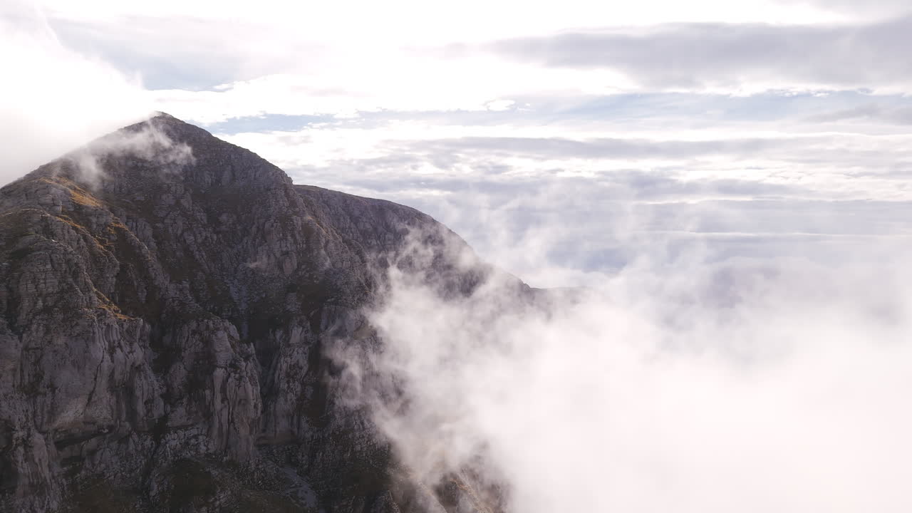 Cloud covered cliffs of Mount Tymfi, captured in a misty aerial establishing view for a mysterious effect, aerial trucking pan hyperlapse