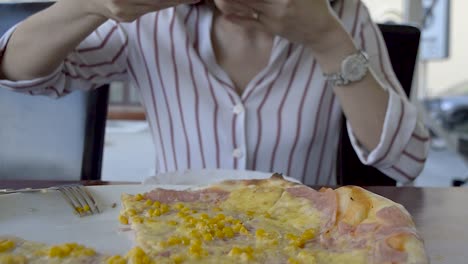 Girl-out-of-focus-eating-a-slice-of-a-huge-pizza-in-front-of-her,-TILT-UP