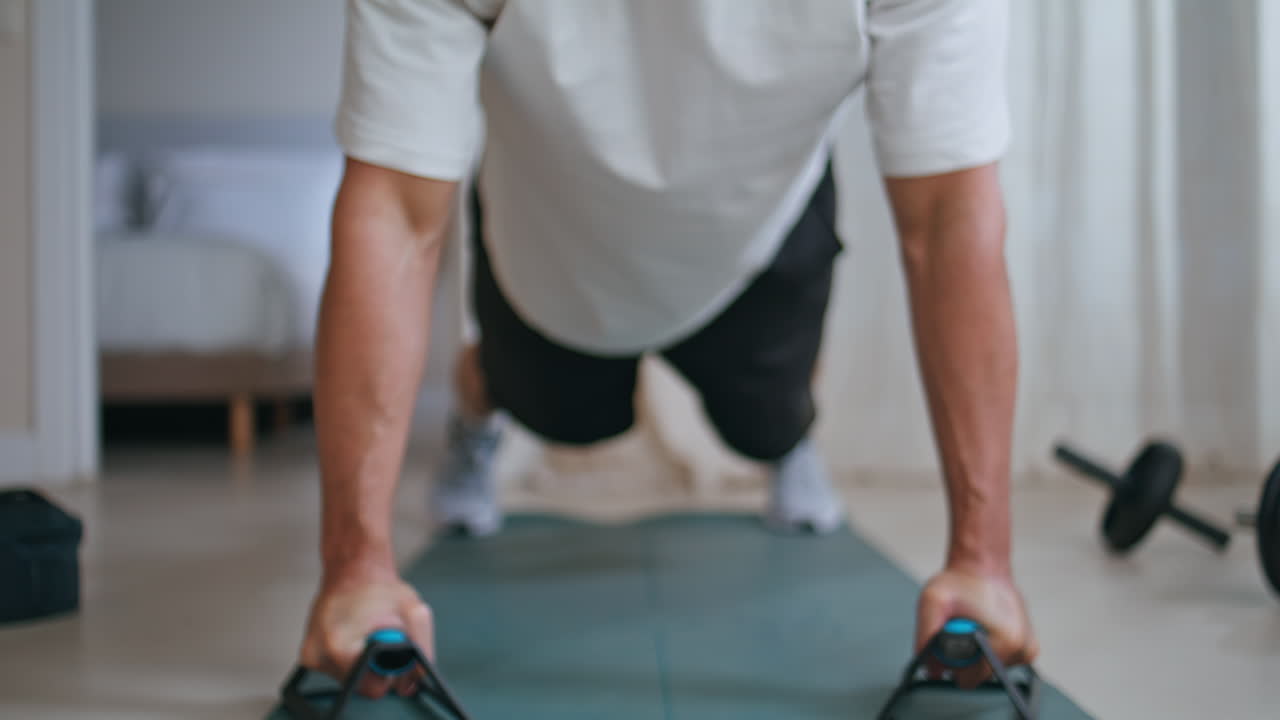 Young sportsman performing pushups with handles at home fitness session closeup