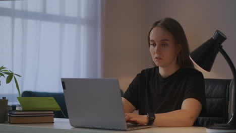 una mujer joven está navegando por internet con una computadora portátil en casa por la noche sentada en la mesa y escribiendo en el teclado comunicándose en redes sociales buscando información en la web