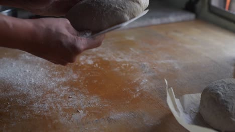 freshly kneaded dough flipped over on wooden kitchen tabletop using white plastic scraping tool, filmed as closeup shot in slow motion style