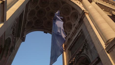 close-up of the european union flag fluttering beneath the grand arch of the cinquantenaire monument in brussels, with a view of the ornate ceiling and warm daylight casting shadows on the stonework