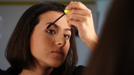 beautiful young woman adding mascara on eyelash in front of mirror, close up