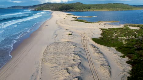 Drone aerial landscape of 4WD off-road vehicle driving along Cellito Beach with Smiths Lake river inlet channel creek bay coastline headland of Pacific Palms Australia travel tourism adventure