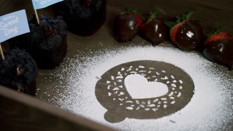 Zoom-into-Making-a-heart-out-of-white-confectionate-powdered-sugar-with-chocolate-covered-strawberries-and-muffins-on-the-side