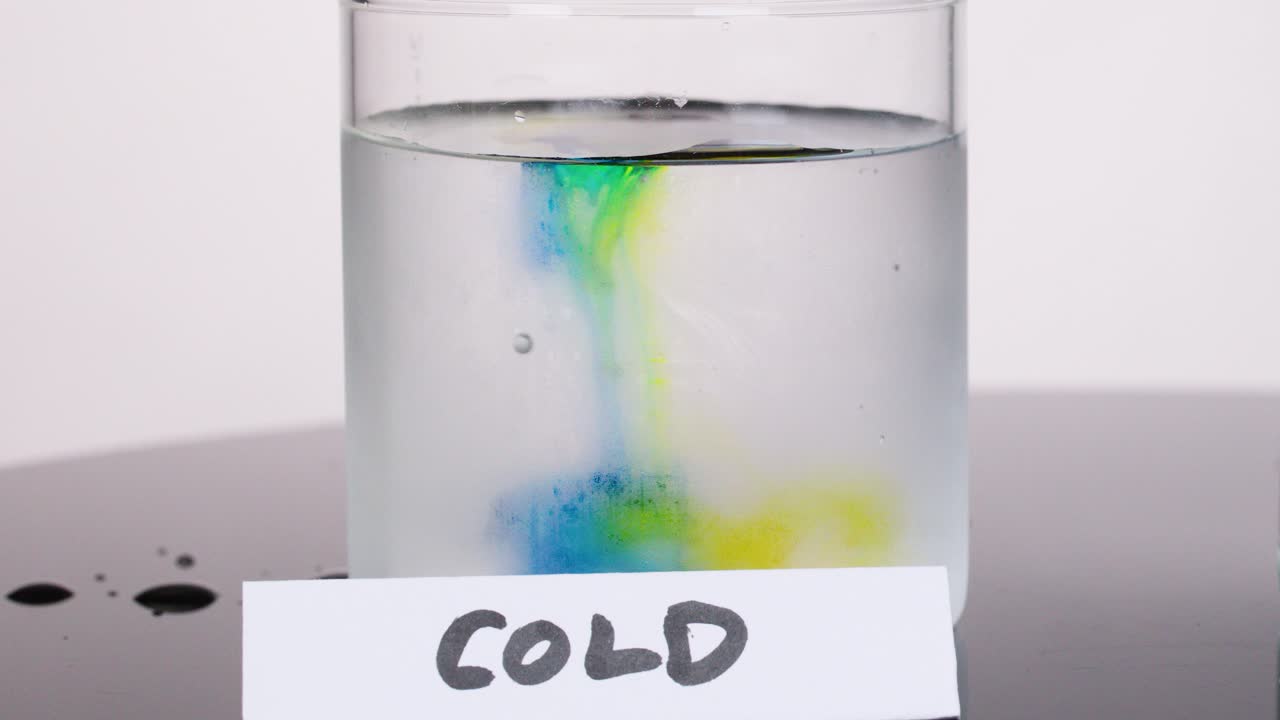 Colored dye slowly disperses in cold water glass, captured with static camera and soft lighting