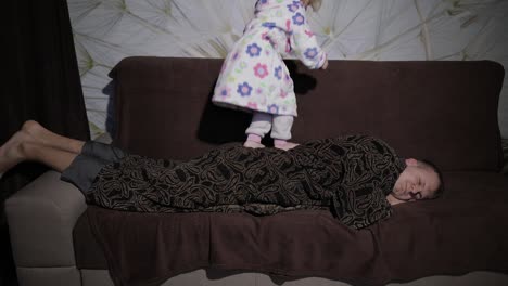 little girl in bathrobe waking her father up. man sleeps on the couch