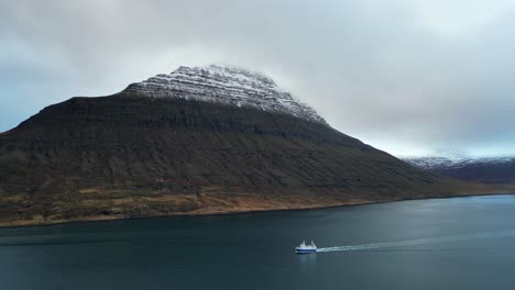 boat sailing in icelandic fjord with snow capped mountain, aerial view