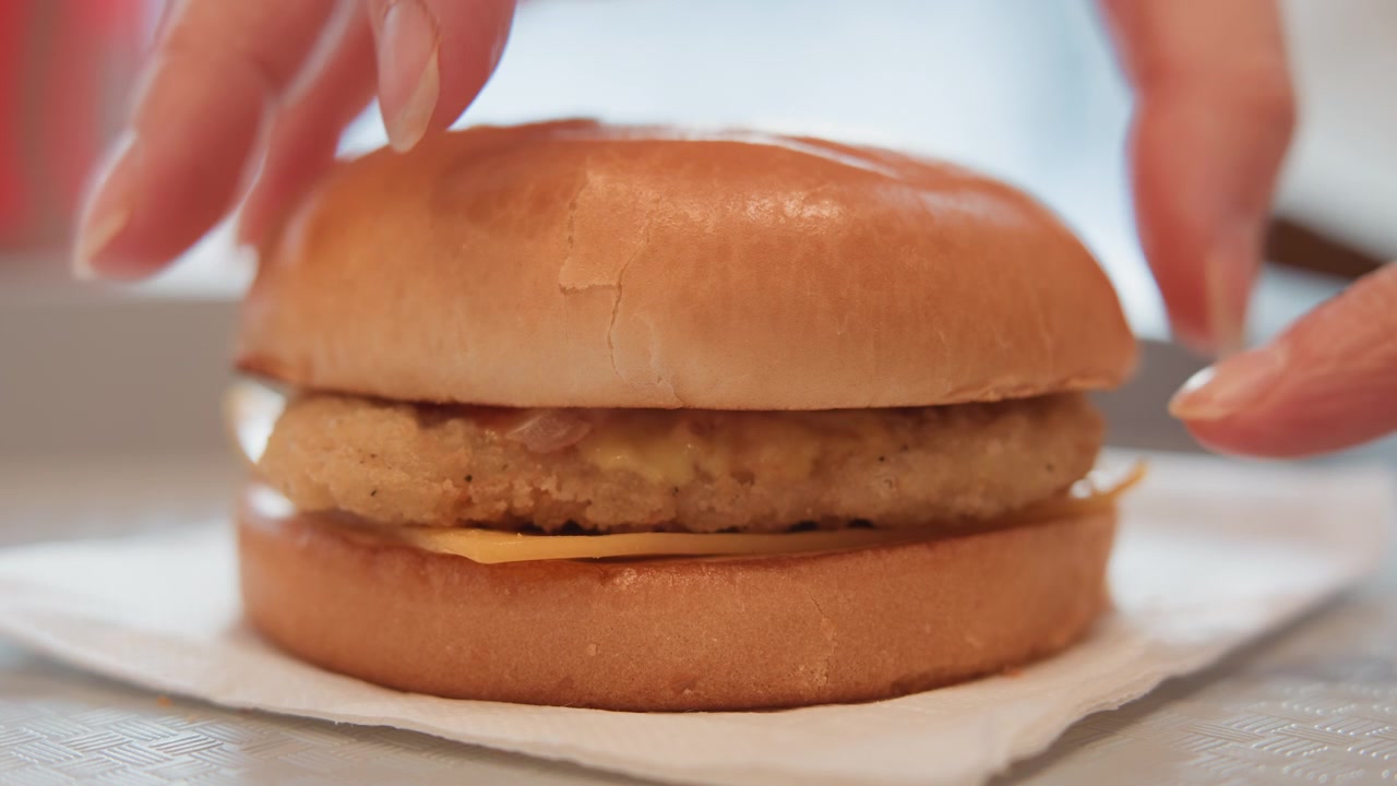 Vista ravvicinata mostra una polpetta rotonda impanata che si solleva sopra un panino inferiore lucido su un tovagliolo di carta, esponendo la base vuota del panino, panatura croccante, riflessi caldi, ombre morbide e una presentazione informale del cibo