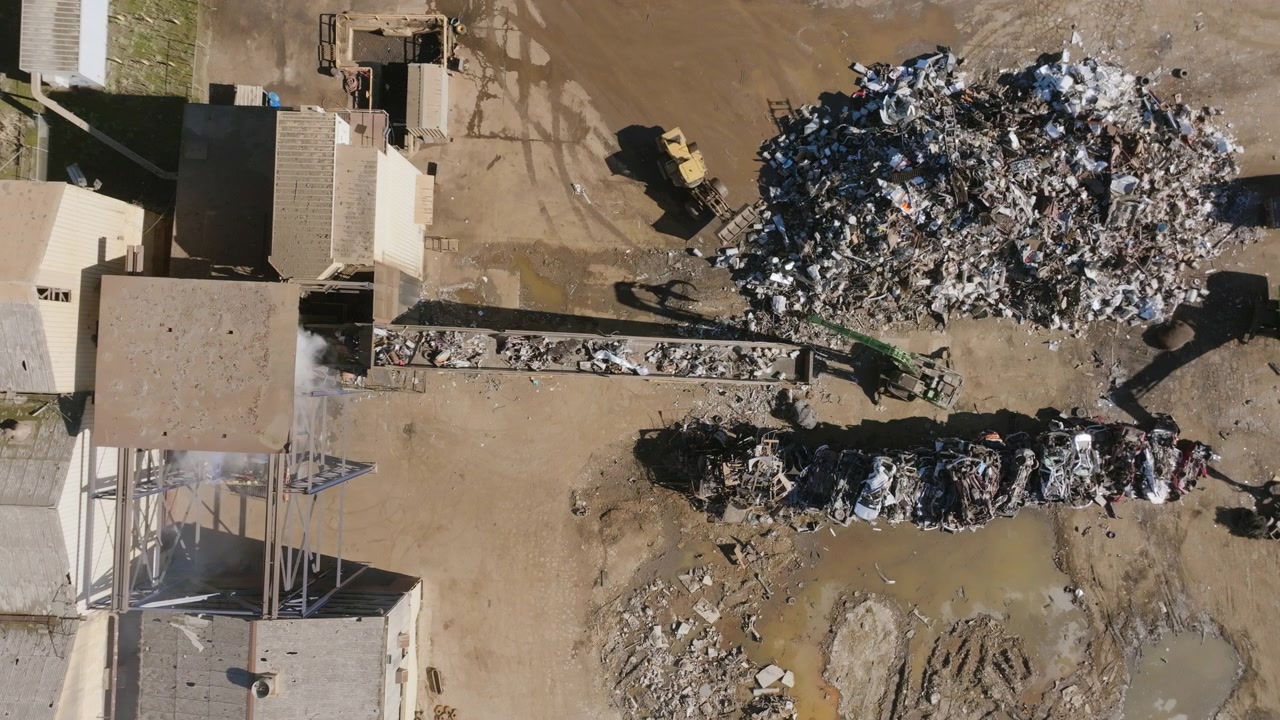 Riprese aeree statiche dall'alto di una terna che sposta rottami metallici su un nastro trasportatore in un impianto di riciclaggio del metallo.