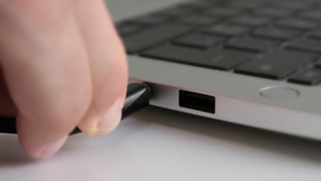 man plugging headphone jack into laptop, close up