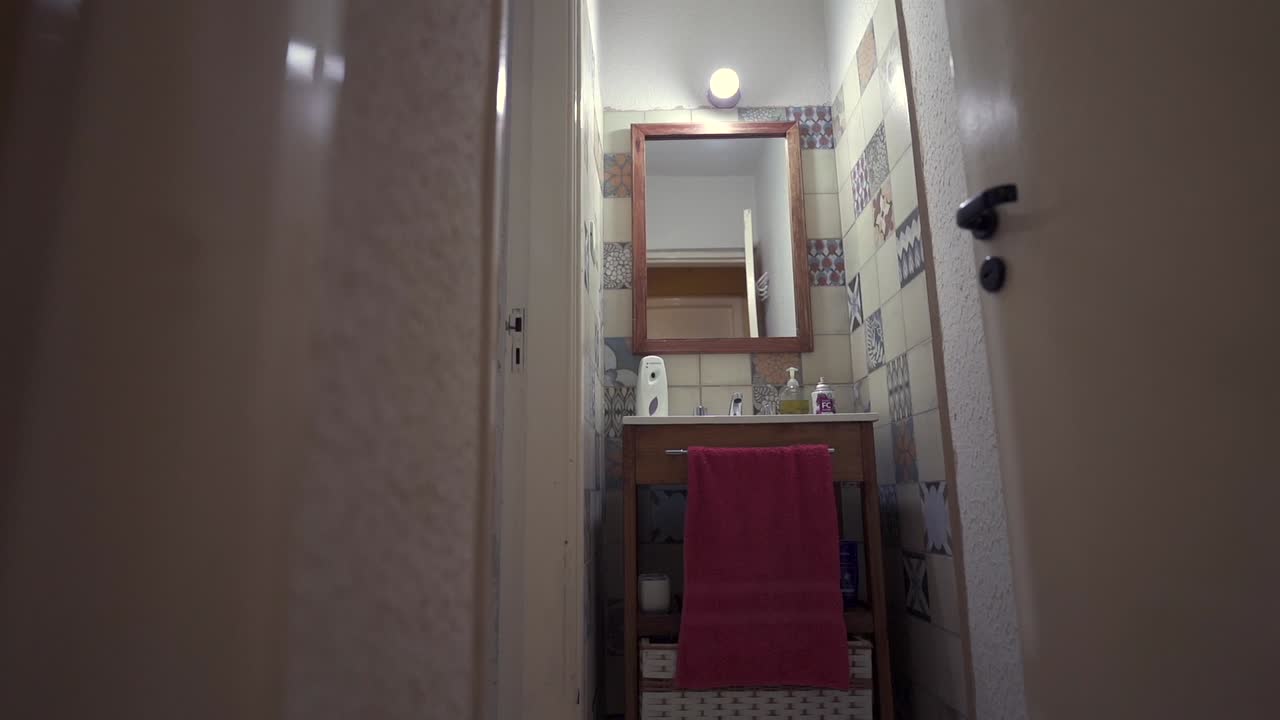 Narrow house bathroom with mirror, sink, towel and patterned tiles under the interior lighting.