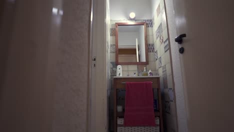 narrow house bathroom with mirror, sink, towel and patterned tiles under the interior lighting.