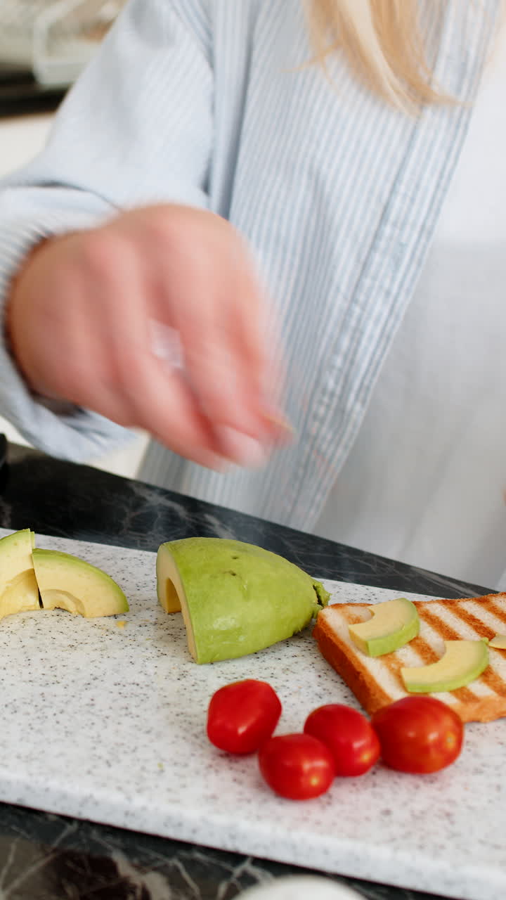 Primer plano de una joven rebanando aguacate para tostadas de tomate en la cocina de su casa, preparando un desayuno saludable.