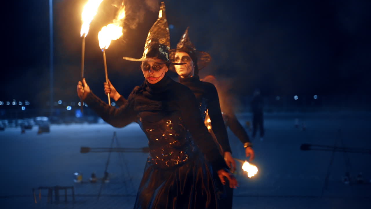 Female actors perform fire show wearing witch costumes. Artistic band shows the fire spectacle outdoors.