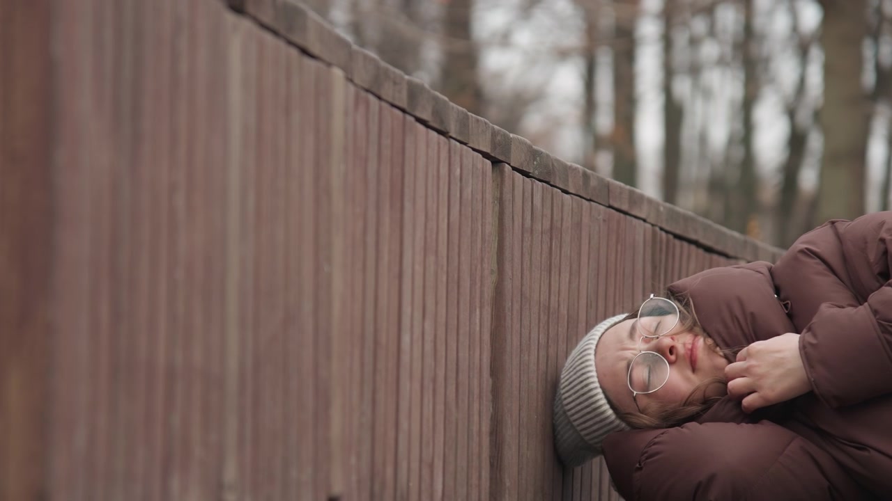 Woman relaxes outside. Solo woman unwinding on chilly park bench. Woman enjoying leisure time outdoors during cold winter weather. Woman peacefully resting on park bench amid cold winter atmosphere