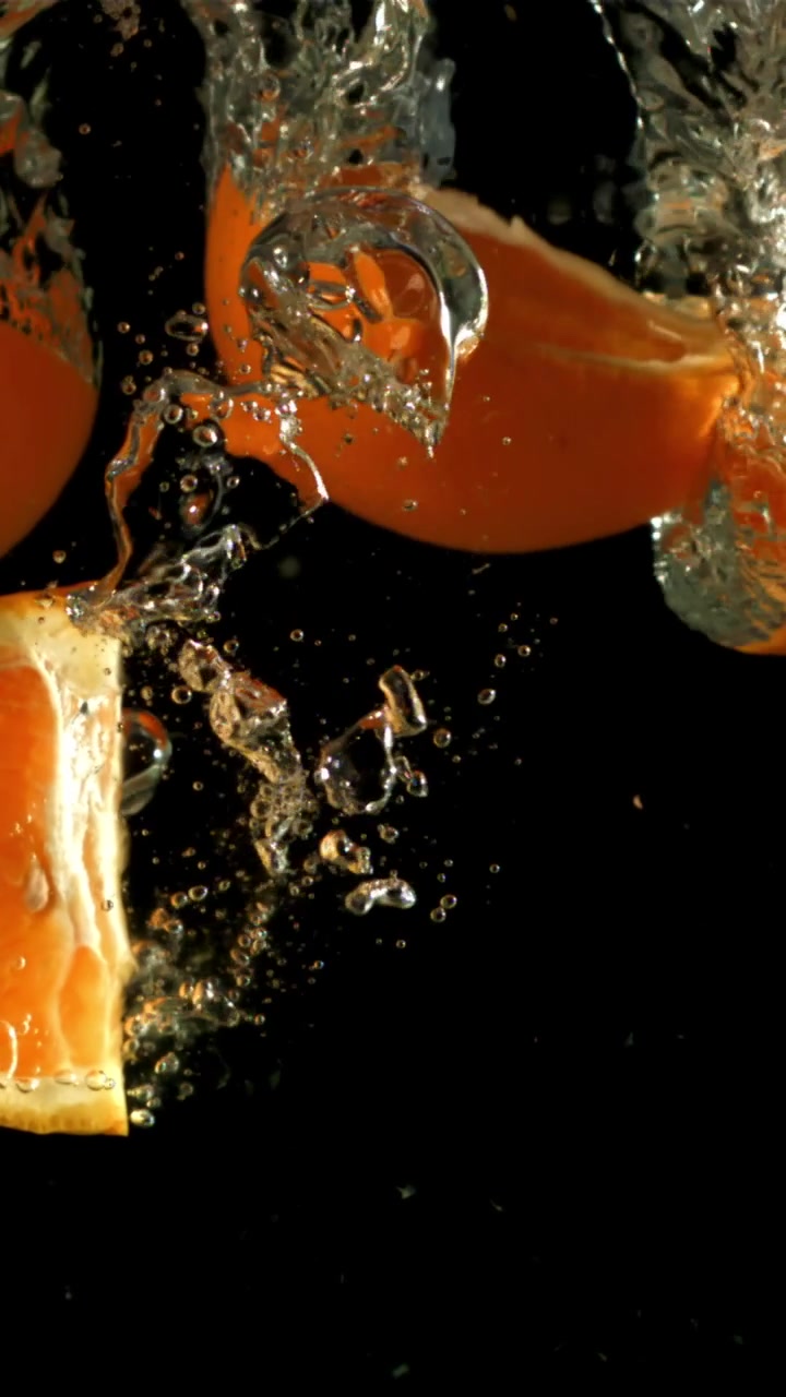 Fette d'arancia fresche e frutta intera che schizzano nell'acqua al rallentatore