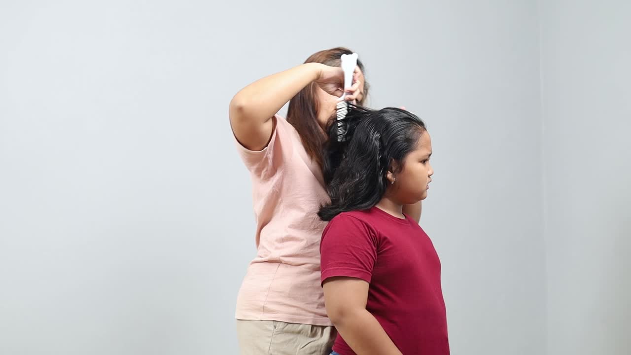 Mother is trying to tie a ponytail, but as she pulling hair, daughter is almost crying