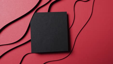 Video-of-close-up-of-square-of-black-paper-on-waves-cut-out-and-copy-space-on-red-background