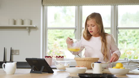 girl wearing pyjamas baking in kitchen at home following recipe on digital tablet