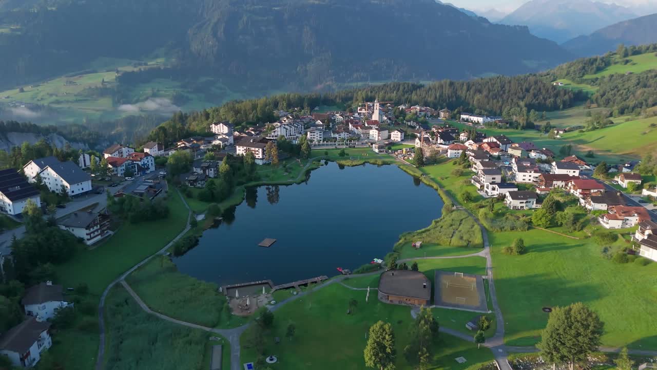 Natural mountain lake of laax town in Switzerland. Sunset time in Switzerland. Aerial view. Small neighborhood located on hilltop in alps. Summer seasons