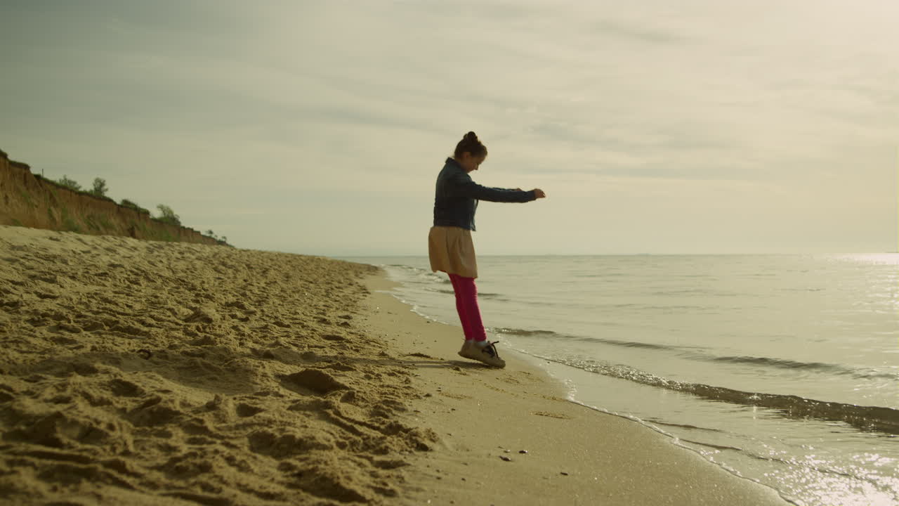 해가 지는 해변에서 야외에서 놀고 있는 작은 소녀. 해변에서 혼자 휴식을 취하는 행복한 아이