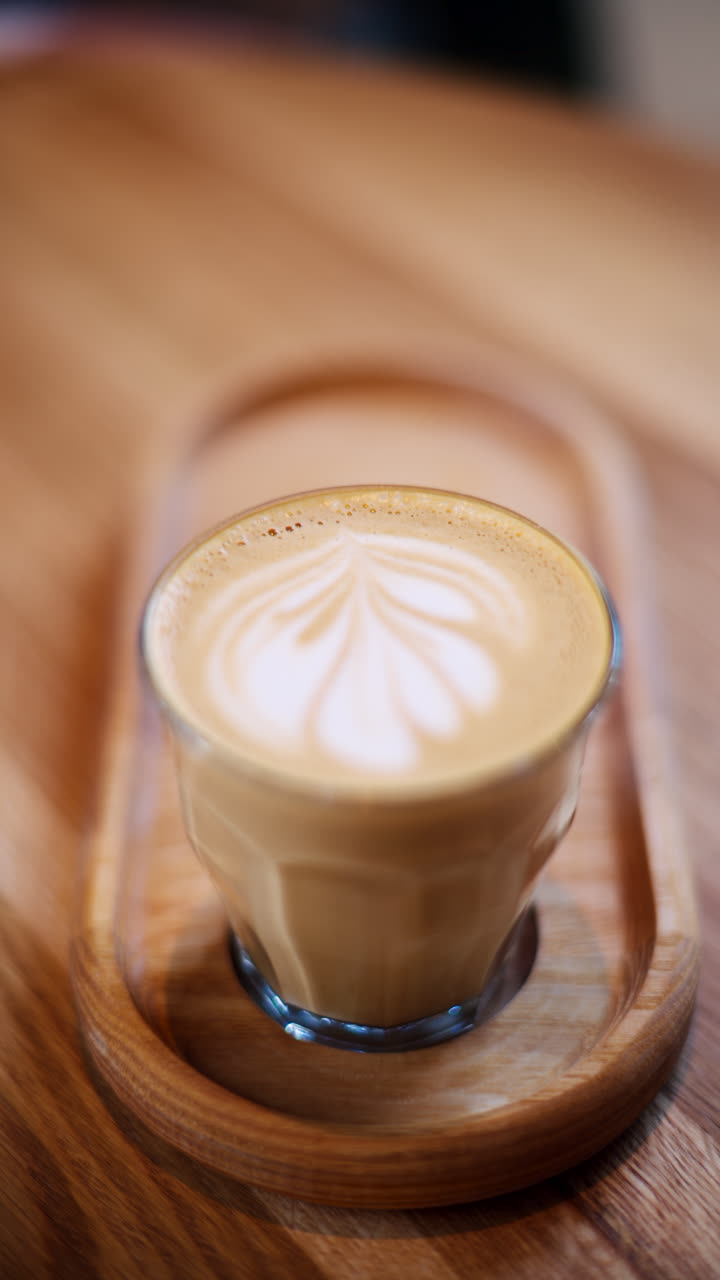 A glass of latte standing on a wooden tray on a table at a cafe. Vertical