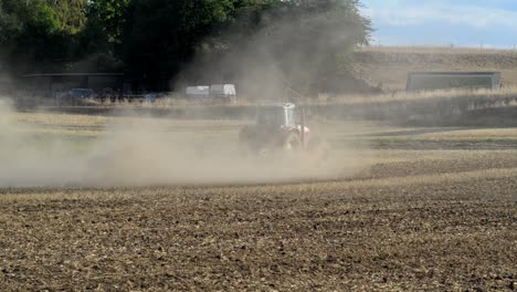 red tractor plowing a dry field after months without rain causing huge amounts of dust being swirled up