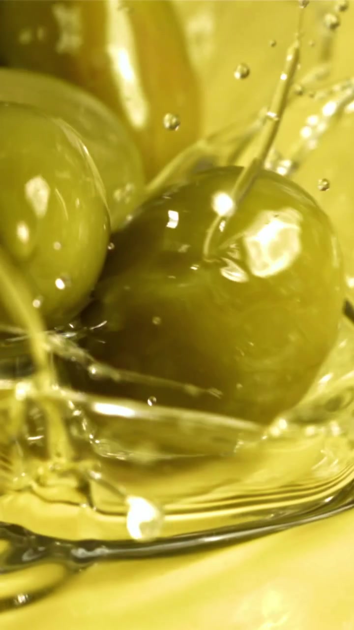 Olive verdi che schizzano in olio d'oliva dorato al rallentatore