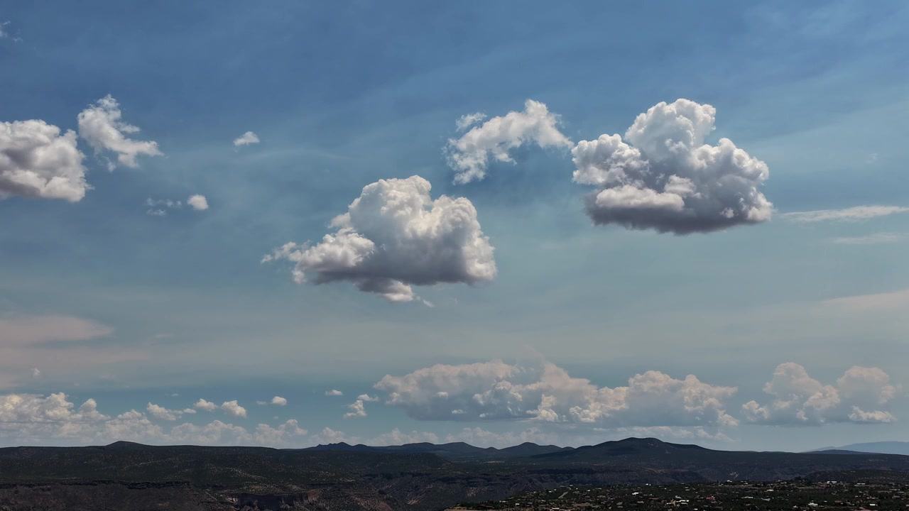 4K drone-timelapse av cumulus-skyer som endrer form mot en blå himmel. De milde, utviklende formasjonene skaper en rolig zen-atmosfære over en vidstrakt sørvestlig ørken og fjerne mørke foten av fjellene