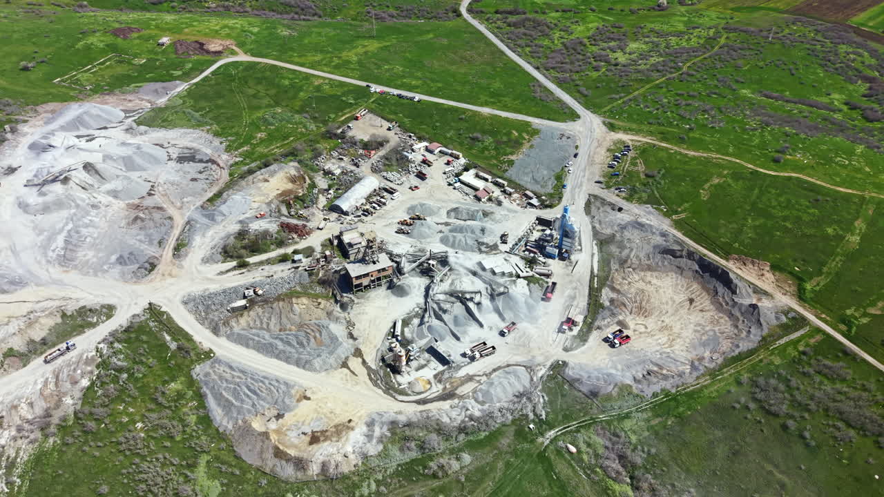 Granite quarry operation with trucks and machinery located in a hilly area under bright sunlight