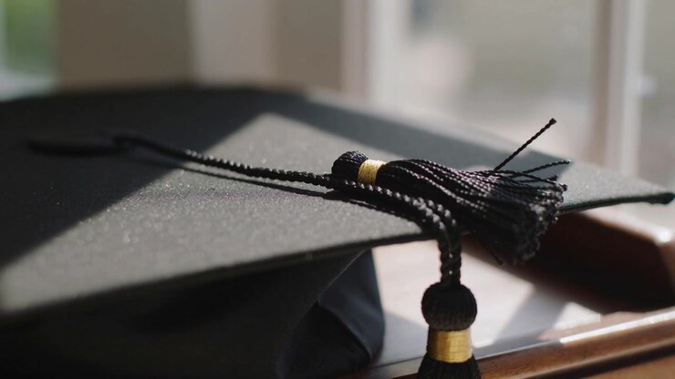 Shifting focus revealing black mortarboard with gold band and tassel moving at window, gown below