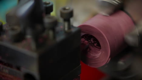 lathe machine hollowing out the center of rotating red cylindrical workpiece in factory. closeup shot, slow motion