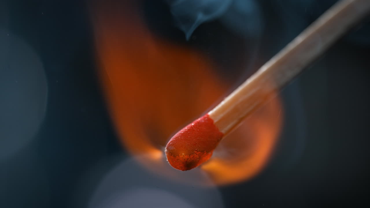 encendido en macro, la cabeza roja de azufre y potasio se quema y emite humo que se eleva sobre un fondo azul