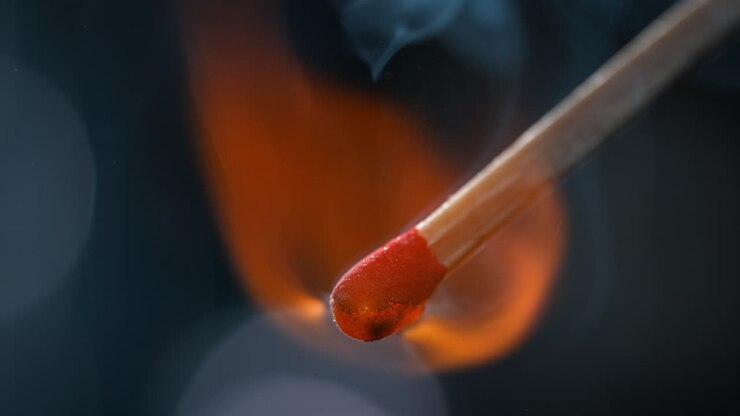 Match Igniting In Macro, Red Sulfur-Potassium Head Combusts And Emits Smoke Rising on a Blue Background