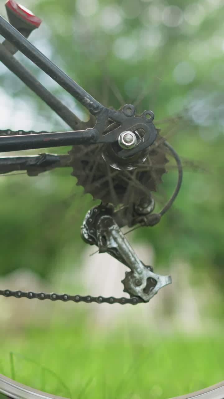 primer plano de la rueda trasera giratoria de la bicicleta y el sistema de engranajes, la rueda gira brevemente con un fondo verde borroso, con una vista parcial del ciclista visible cerca de la bicicleta
