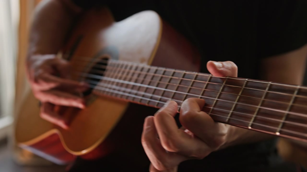 Primo piano di una persona che suona una chitarra classica acustica, eseguendo un assolo al rallentatore usando la tecnica fingerstyle. Il video presenta una bellissima illuminazione realistica e calda e un'ottima qualità estetica visiva.