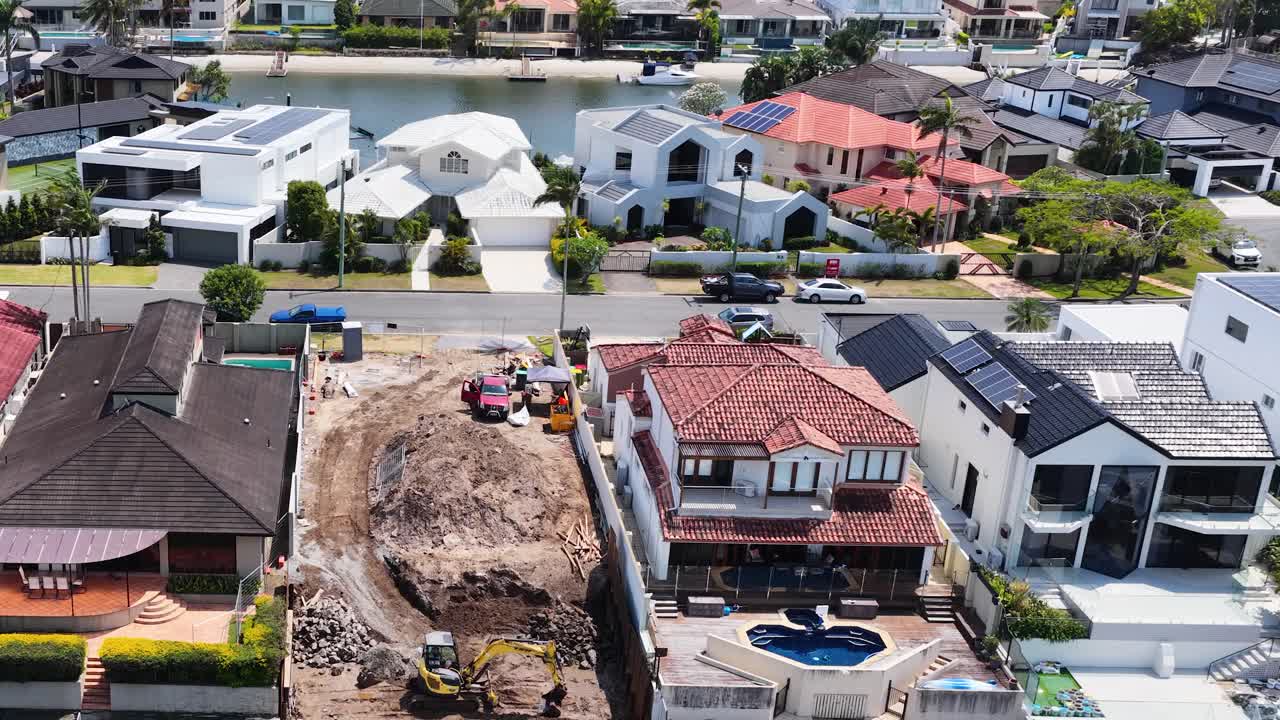 Daytime drone flyover of waterfront homes, swimming pools, and active residential construction site in Australia