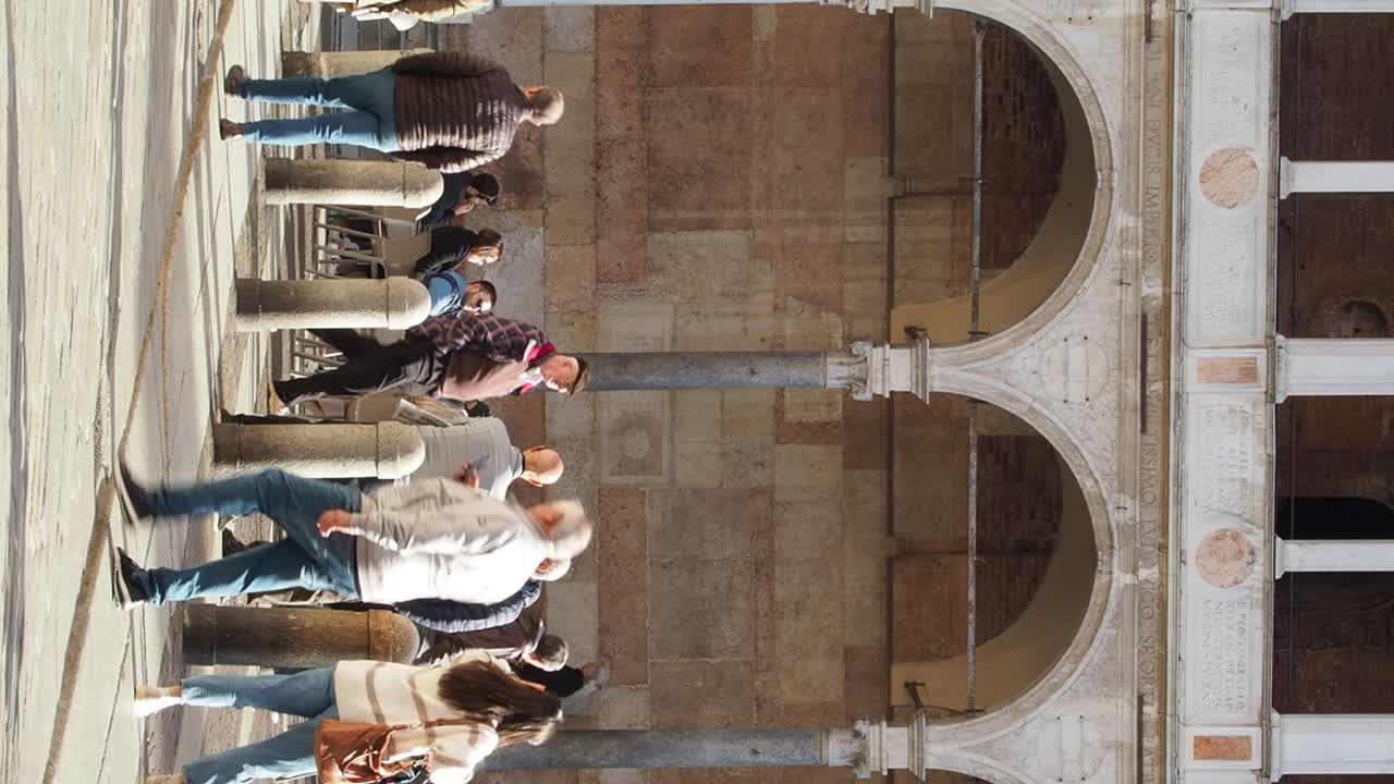 Locals and Visitors strolling through the duomo square beneath the arches of the cathedral, Cremona, italy