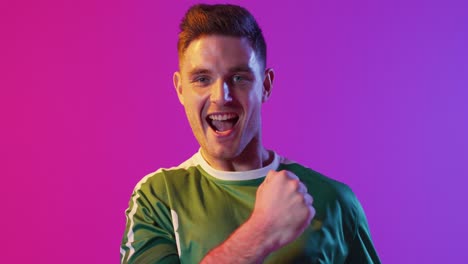 retrato de un feliz jugador de fútbol masculino caucásico levantando las manos sobre la iluminación rosa neón