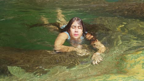 young girl in a blue bikini in a plunge pool at a waterfall on a sunny day