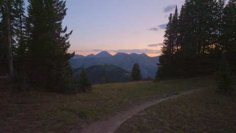 push over hiking trail and past trees towards mountain range in the colorado rockies on a beautiful evening at sunset